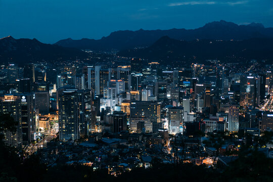 Cityscape of Seoul, South Korea lit up at dusk, with Mountains behind.