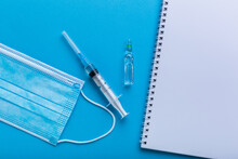 A Syringe With Vaccine On Blue Background With A Protective Face Mask And White Black Note For A Prescription. Notes For People Who Want To Make Vaccination.