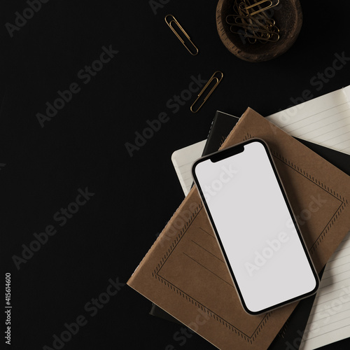 Obraz Dibond Flatlay of blank screen mobile smart phone, notebooks, clips in wooden bowl on black background. Home office desk workspace. Business, work template. Flat lay, top view.