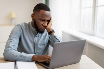 Unhappy Black Businessman Looking At Laptop Sitting At Workplace Indoor