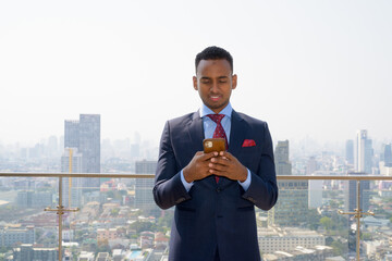 Wall Mural - Portrait of handsome young African businessman wearing suit while smiling and using mobile phone