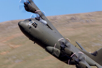 Lockheed C-130 Hercules flying low level in the UK. Four engines turboprop transport and cargo plane low level in a valley