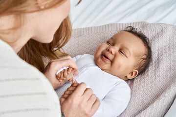 caucasian mum, foster single parent holding hands of happy cute adorable adopted infant african amer