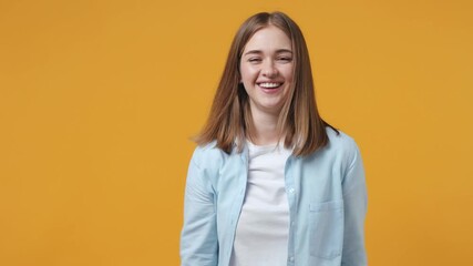 Wall Mural - Cheerful funny blonde young woman 20s in blue shirt posing isolated on yellow background in studio. People lifestyle concept. Doing dab hip hop dance hands move gesture youth sign hiding covering face