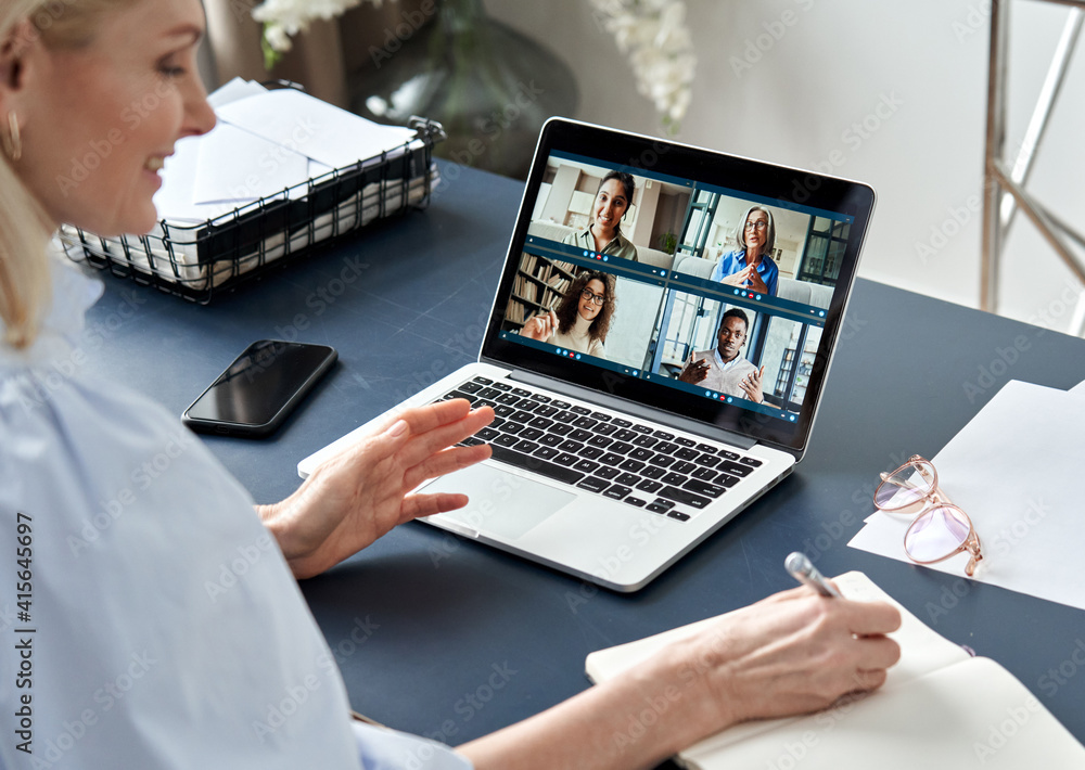 Business woman having virtual team meeting on video conference call using laptop computer. Social distance work from home office with diverse people group in remote online chat. Over shoulder view Stock Photo |