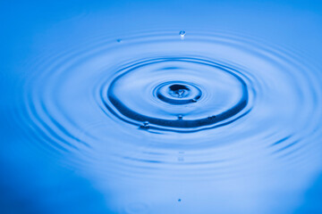 Close up view of Drops making circles on blue water surface isolated on background.