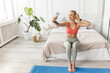 © shunevich - A young yoga instructor sits on a bed and speaks via video communication, resting from workouts, a fit athlete in sportswear uses a mobile phone while waiting for a workout in a fitness studio.