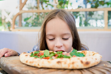 Hungry kid girl 5-6 years eating pizza  on  cafe terrace on sunny day. Family having fun outside the restaurant. 