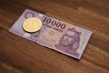 Wall Mural - Hungarian forint 10000 forint banknote Saint István King. Brown wooden table. Next to it is a gold bitcoin digital cryptocurrency coin. Bank image and photo.