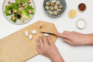 woman chef is cooking, making diet homemade caesar salad, step by step instruction. Step 2 - cutting quail eggs, adding them to the bowl