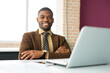 © Alexandr - handsome young african man in suit at table in office with laptop