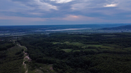 Poster - Aerial view of dense forests with green trees and buildings near the river under the cloudy sky