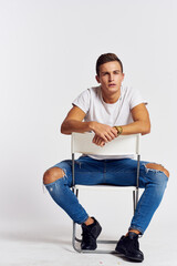 Wall Mural - A man in jeans sits on a chair backwards and and ripped jeans T-shirt front view