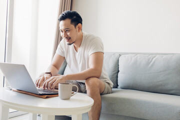 Happy Asian man is working on his laptop in the living room.