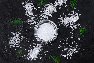 Wall Mural - Coarse salt crystals on a black table. Bowl with sea salt. Background for advertising salty.