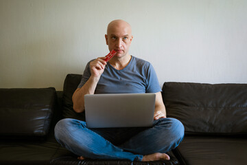 Emotional bald man on the couch with a laptop and credit card in his hand. Online shopping concept