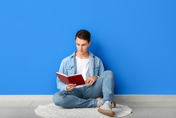 Wall Mural - Young man reading book near color wall