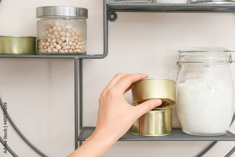 Woman taking metal can from shelf in kitchen