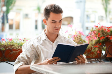 Wall Mural - Young man reading book in outdoor cafe