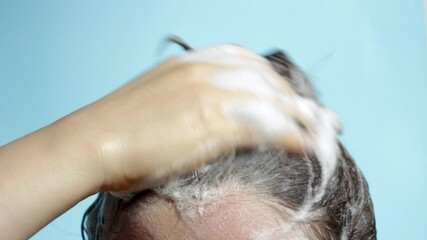 Wall Mural - The girl washes off shampoo from head close-up on blue background.