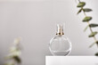 Glass perfume bottle on white podium. Floral eucalyptus arrangement. Minimal mockup style, soft focus