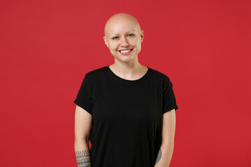 Young bald smiling caucasian cheerful friendly positive attractive tattooed woman 20s without hair wearing black basic casual t-shirt looking camera isolated on red color background studio portrait.