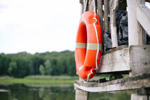 Old Red Inflatable Lifebuoy Hangs On A Wooden Pier By The Lake Water