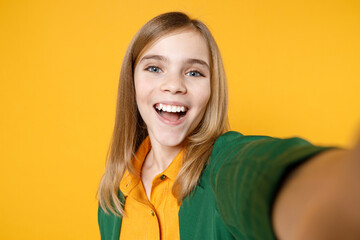 Wall Mural - Close up little blonde kid smiling cute girl 12-13 years old in casual clothes do selfie shot on mobile phone look camera isolated on yellow background children studio Childhood lifestyle concept.