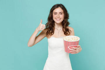 Wall Mural - Smiling bride young woman 20s in beautiful white wedding dress hold bucket of popcorn showing thumb up like isolated on blue turquoise background studio portrait. Ceremony celebration party concept.