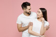 © ViDi Studio - Young happy couple in love two friends man brunette woman 20s in white basic t-shirts looking to each other standing smiling hugging embrace isolated on pastel pink color background studio portrait.