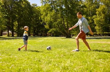 Wall Mural - family, fatherhood and people concept - happy father and little son with ball playing soccer at summer park