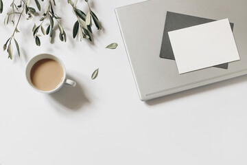 Summer working space composition. Blank greeting card, envelope mock-up scene. Cup of coffee, olive tree branches and laptop isolated on white table background. Flat lay, top view. Home office.