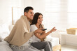 © New Africa - Happy couple covered with warm beige warm plaid watching television indoors