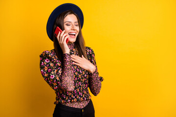 Poster - Portrait of funny lady closed eyes laughing speak phone dark retro headwear isolated on yellow color background