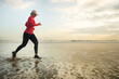 fit and attractive mature woman with grey hair doing beach workout on her 50s running on the beach happy and free in senior fitness selfcare and wellness concept