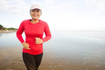 fit and attractive mature woman with grey hair doing beach workout on her 50s running on the beach happy and free in senior fitness selfcare and wellness concept