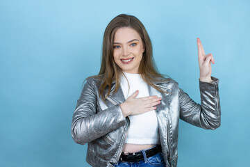 Pretty woman with long hair wearing a casual jacket over blue background smiling swearing with hand on chest and fingers up, making a loyalty promise oath