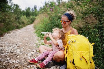 Wall Mural - mother with small toddler daughter hiking outdoors in summer nature, resting.