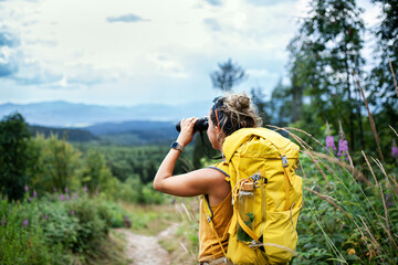 rear view of woman hiker with backpack on a hiking trip in nature, using binoculars.