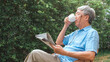 © tirachard - Asian senior men relax at home. Asian Senior Chinese male enjoy rest time wear glasses read newspaper and drink coffee while lying in the garden at home in the morning concept.
