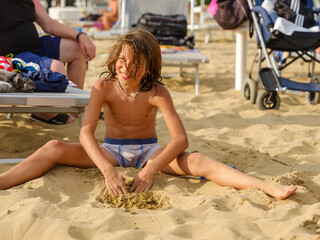 The child in a bathing suit plays on the sand at the beach on a sunny day.