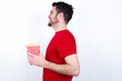 © Jihan - Profile of smiling young handsome man in red T-shirt against white background eating popcorn with healthy skin, has contemplative expression, ready to have outdoor walk.