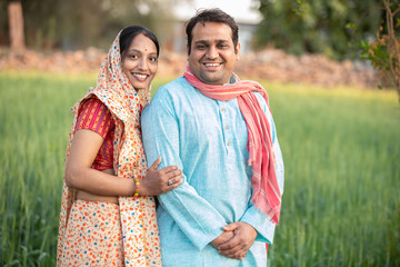 Wall Mural - Portrait of happy young indian farmer couple at agricultural field. man wearing kurta and woman wearing sari looking at camera 