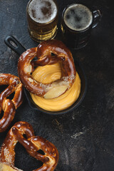 Wall Mural - Cheese dip, pretzels and beer over dark brown stone background, vertical shot, high angle view with space