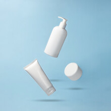 White Jar And Bottles For Cosmetics Products Flying On Blue Background. Levitation. Body Care Creative Concept. Mock Up