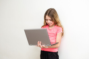 Young caucasian girl standing at the wall and working with laptop. Child and technology concept with copy space.