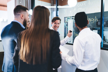 Wall Mural - Group of positive colleagues standing near glass with business scheme