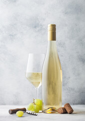 Glass and bottle of summer white wine with grapes, corks and corkscrew on light background.