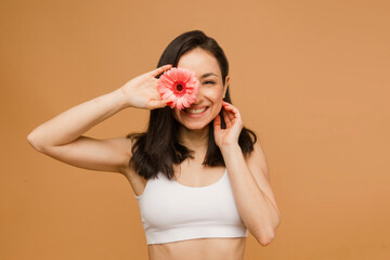 Wall Mural - Fit and sporty female in underwear. Beautiful and healthy woman covers eye up with flowers over beige background. Sport, fitness, diet, weight loss and healthcare concept