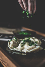 Homemade Dumplings Sprinkled With Fragrant Greens. They Lie On A Wooden Tray In Dark Utensils. Warm Muted Colors.